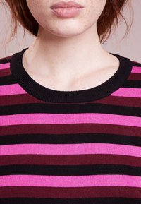 Maglione a righe con texture a costine, caratterizzato da bande orizzontali di rosa, rosso scuro e nero. Collo rotondo, design aderente.