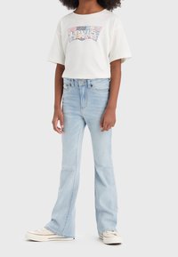 Bílý tričko s krátkým rukávem a barevným logem Levi's, spárované se světle modrými rozšířenými džíny. Nosené se světlými teniskami.