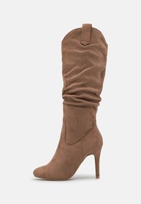 Botte haute en daim marron avec tige détendue et bout pointu, équipée d'un talon stiletto haut et d'une languette à l'arrière.