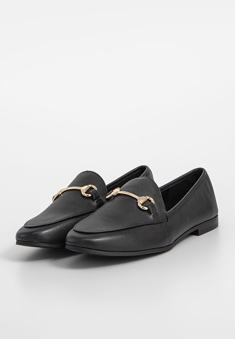 Mocasines de cuero negro con punta afilada, suela plana y un acento de hardware en tono dorado a lo largo de la parte superior como detalle decorativo.
