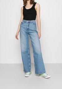 Lösa, ljusblå jeans med hög midja, kombinerat med en svart linne med volangdetaljer. Vita och gröna sneakers fulländar looken.