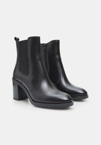 Botas de cuero negras hasta el tobillo con punta afilada, paneles laterales elásticos y tacón sólido. Textura suave y diseño minimalista.