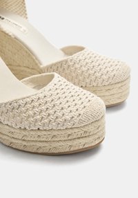 Beige espadrille-kilklackar med en vävd textilöverkinn och en repomslutande plattform. Öppen tå-design med en slät inredning och stickade detaljer.