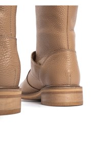 Kawowe skórzane buty z teksturowanym wykończeniem, niskim obcasem z warstwowymi drewnianymi akcentami oraz widocznymi szwami wzdłuż szwów.