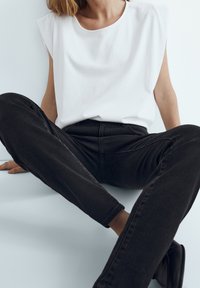 Haut sans manches en coton blanc avec col rond, associé à un jean en denim noir. Tissu au toucher lisse et design à jambe droite. Chaussures non visibles.