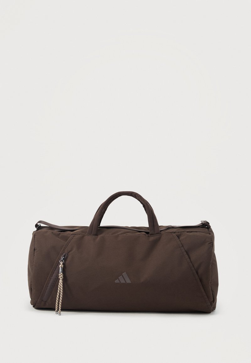 Tamnosmeđa Adidas torba tipa duffel s dvostrukim ručkama, glavnim pretincem na patentni zatvarač te prednjim džepom na patent s pletenim vrpcama na patentnom zatvaraču.