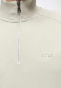 Pull beige à demi-fermeture éclair avec col côtelé et logo « BOSS » embossé sur la poitrine gauche.