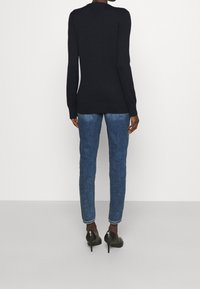 Tmavě modrý svetr s dlouhým rukávem s žebrovanými manžetami a lemem, doplněný světle modrými úzkými džíny a černými botami na podpatku, zobrazený zezadu.