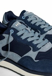 Een paar marineblauwe en grijze suède sneakers met lichtgrijze veters en een cushioned zool, die gedetailleerde stiksels en stofstructuur laten zien.