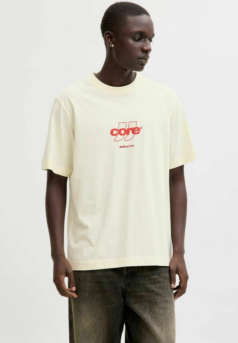 T-shirt en coton jaune clair avec un motif rouge central comprenant le texte "core" et un logo. Manches courtes et coupe décontractée.