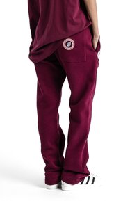 Pantalon de survêtement bordeaux avec une coupe décontractée, doté de poches latérales et d'un patch logo au dos. Matière en coton avec une texture douce.