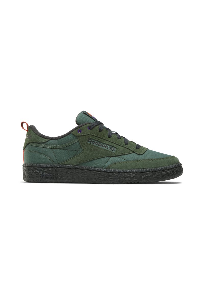 Green suede low-top sneakers with black rubber sole, contrasting purple eyelets, and a red heel pull tab. Features textured panels and logo.