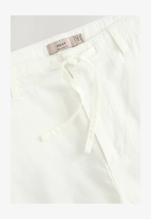 Białe spodnie o luźnym kroju z elastycznym paskiem i subtelną teksturą. Wyposażone w metkę z informacją o marce wszytą w talii.