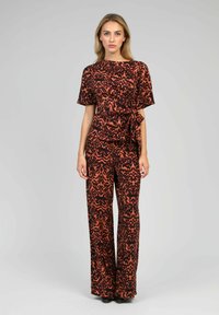 Combinaison noire et orange à motifs avec des manches courtes, une taille ceinturée, des jambes larges et une texture de tissu lisse.