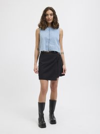 Lys blå cropped denim-top med rå kant, kombinert med et svart omslagskjørt. Svart knelange støvler med tykk såle fullfører antrekket.
