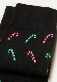 Sorte sokker med et gentaget mønster af røde og grønne slikstænger, strikket med hvide detaljer og en glat tekstur.