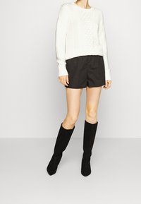 Biały dzianinowy sweter z warkoczowym wzorem, czarne szorty i czarne kozaki do kolan z ostrymi noskami.