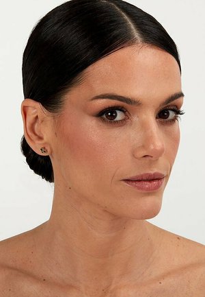 Goldene Steckerohrringe mit einem grünen Stein, kreisförmiges Design, getragen von einer Person mit einer schlichten Frisur und dezentem Makeup.