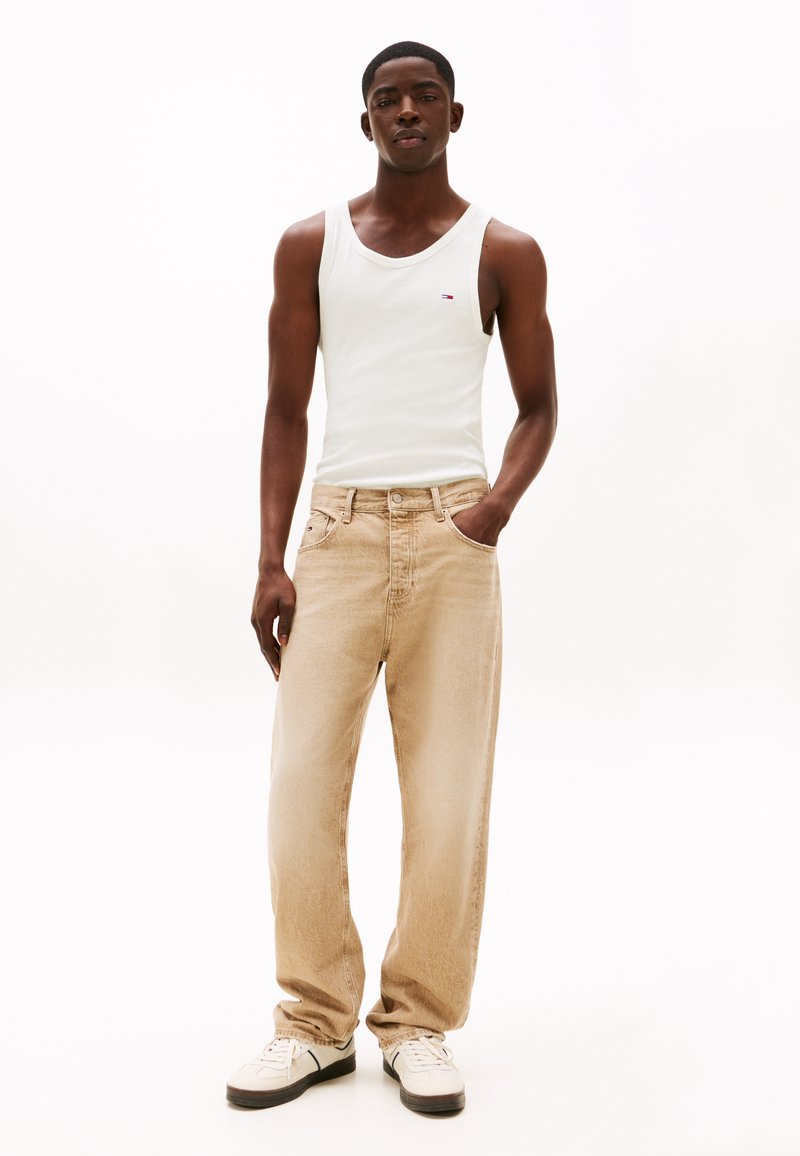 Débardeur en coton blanc, jean en denim beige à coupe décontractée, texture légère, et baskets blanches avec des accents noirs.