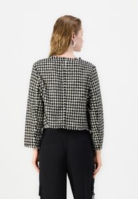 Sacou scurt dintr-un material texturat, cu un model houndstooth alb-negru, cu mâneci lungi și închidere cu buton la spate.