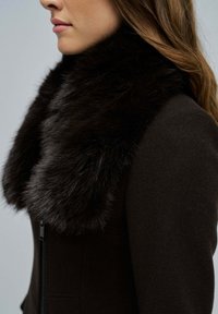 Abrigo marrón oscuro con un lujoso cuello de piel negro; diseño ajustado con cremallera lateral y textura suave, resaltando la apariencia lujosa del cuello.