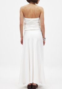 Robe blanche en satin sans bretelles avec une jupe fluide, présentant une texture lisse et un corsage ajusté. Associée à des chaussures plates marron foncé.
