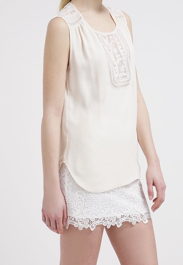 Blouse sans manches crème avec un panneau en dentelle détaillé à l'avant et un ourlet festonné. Associée à un short en dentelle blanche avec un motif floral.