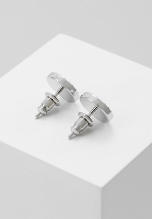 Paar runde silberne Metallstecker mit Steckverschluss, platziert auf einer weißen schrägen Oberfläche.