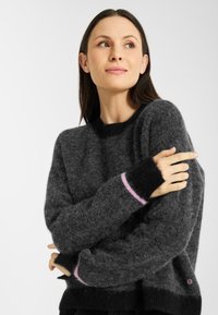 Donkergrijze, pluizige sweater met zwarte accenten en een roze streep bij de boorden. Ronde hals, relaxte pasvorm, met een cirkelvormig logodetail.