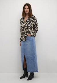 Black blouse with white floral pattern, paired with a light blue denim maxi skirt featuring a front slit. Black ankle boots complete the look.