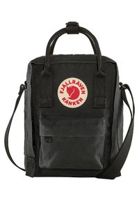 Svart Kånken-ryggsäck med rektangulär form, tygmaterial, framficka med dragkedja och en rund röd logotyp. Har handtag upptill och en justerbar rem.
