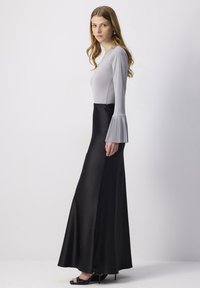 Top gri lung cu mâneci clopot plisate, purtat cu o fustă neagră, fluidă, de lungime până la podea. Texturi netede, siluetă elegantă.