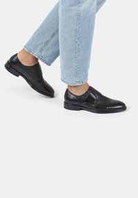Zapatos de vestir de cuero negro con un acabado suave, que presentan una punta redondeada, un detalle de hebilla minimalista y un diseño de tacón bajo.