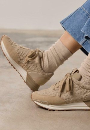 Scarpe sportive beige con tomaia in tessuto testurizzato e suola in gomma liscia. Presentano lacci e dettagli di marca discreti. Abbinate a calze a coste.