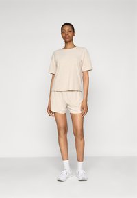 Haut à manches courtes côtelé beige clair et short assorti, fabriqués en tissu doux. Associés à des chaussures de sport blanches et des chaussettes.