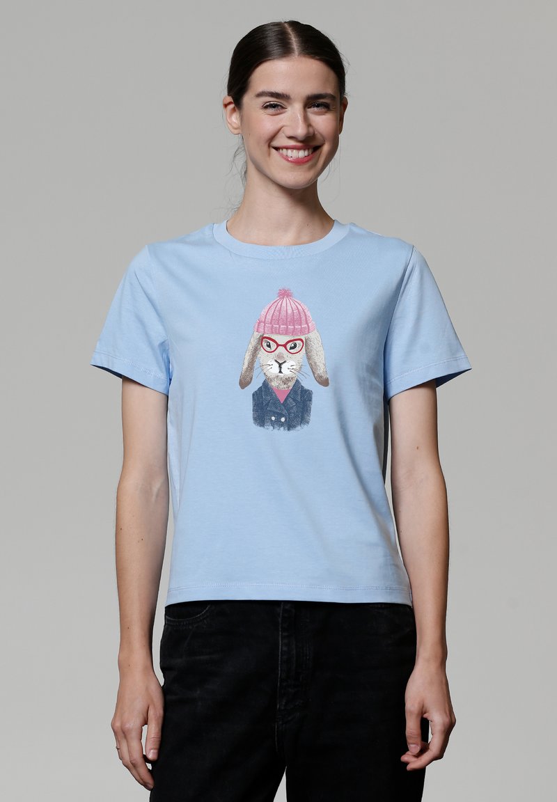 T-shirt en coton bleu clair avec une illustration de lapin portant un bonnet rose et des lunettes, sur un fond simple. Manches courtes, col rond.