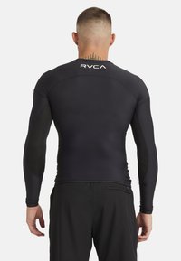 Zwarte rash guard met lange mouwen en een aansluitend ontwerp, met het RVCA-logo op de achterkant. Het gladde, lichte materiaal zorgt voor een elegante uitstraling.