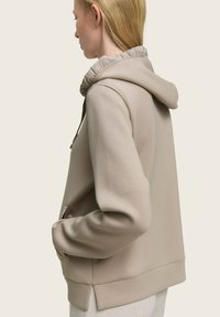 Beige hoodie met een zachte textuur, uitgerust met een geribbelde capuchon, een kangoeroe-pocket en een ontspannen pasvorm met een iets langere achterzoom.