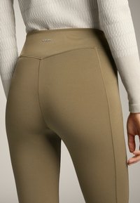 Magas derekú, olívazöld leggings sima, rugalmas anyagból. Diszkrét logóval és karcsú, testhezálló kialakítással rendelkezik.