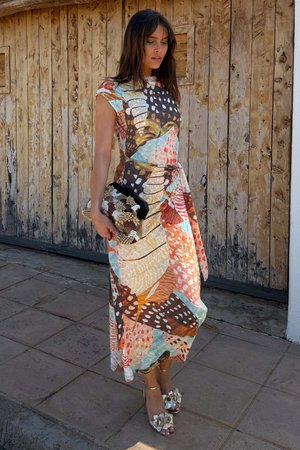 Long, patterned dress with vibrant colors (brown, orange, blue, red) and abstract designs. Accessories include a textured black clutch and embellished sandals.