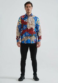 Chemise à motifs colorés avec des designs bleus, rouges et floraux, rehaussée d'accents en imprimé léopard ; à boutons, avec des manches longues, texture du tissu visible.