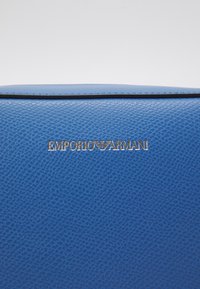 Superficie in pelle texturizzata blu con il logo dorato di Emporio Armani centrato su di essa.