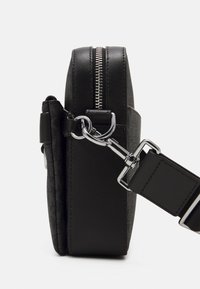 Zwarte handtas met gemêleerde stof en gladde leren accenten, voorzien van een zilveren rits en een verstelbare hengel.
