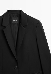 Schwarzer Blazer aus glattem Stoff mit Reverskragen, einem einzelnen Knopfverschluss und zwei vorderen Taschen. Innenlabel sichtbar.