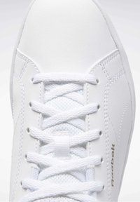 Gros plan sur une basket blanche Reebok montrant les lacets, la languette en mesh et la tige en cuir cousu.