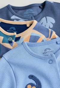 Tre capi d'abbigliamento per neonati: tessuto a coste in navy, blu e un motivo pastello. Uno presenta una decorazione a ricamo di dinosauro e chiusura con bottoni.