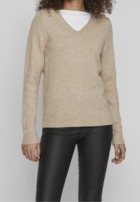 Beige V-halsad tröja i ett mjukt, strukturerat tyg, med ribbade ärmslut och nederkant. Matchad med enkla svarta läderbyxor.