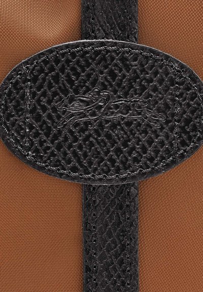 Brown fabric with a black textured leather oval accent featuring a logo, stitched edges, and a smooth finish.
