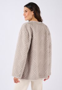 Lichtbeige bontjas met een gestructureerd ruitpatroon, brede mouwen en een relaxte pasvorm. De stof lijkt zacht en pluizig.