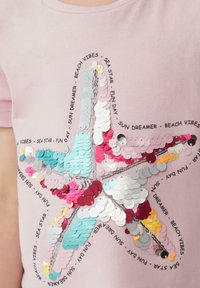 Roze t-shirt met een zeesterontwerp van kleurrijke pailletten, verfraaid met zwarte tekst rondom de ster, wat een textuur effect biedt.